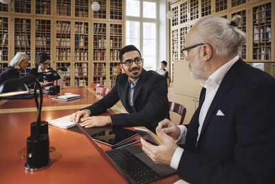 Smiling man discussing with senior lawyer at table in library