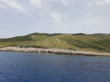 Scenic view of sea by mountain against sky