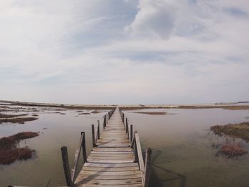 Wooden pier on jetty leading towards sea against sky