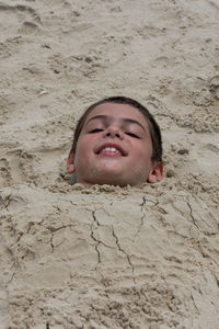 High angle portrait of boy buried in sand at beach
