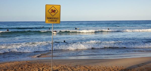 Warning sign on beach against clear sky