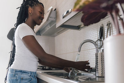 Smiling woman filling water in glass bottle at home