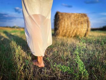 Woman in white dress walking barefoot towards a haystack on the field