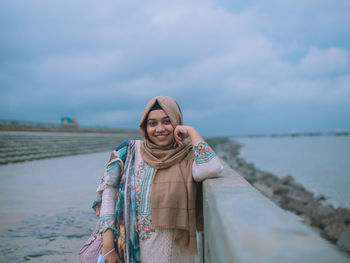 Portrait of smiling young woman standing against sky