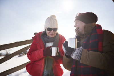 Happy mature couple with hot drinks outdoors in winter