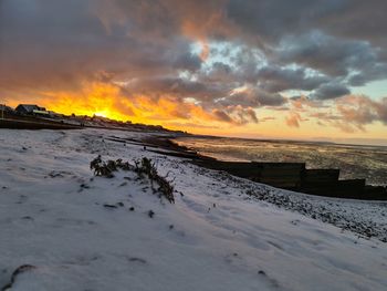 Scenic view of snow covered  beach against sky during sunset