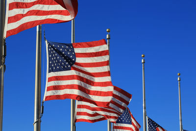 Low angle view of american flags against clear blue sky