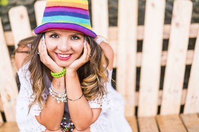 Portrait of beautiful woman wearing multi colored sun hat while sitting with head in hands on bench