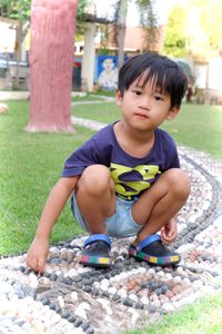 Cute boy crouching on footpath at park