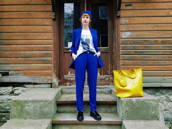 Full length portrait of woman standing against yellow wall