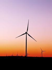 Silhouette wind turbines on field against sky during sunset