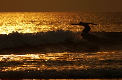 Man surfboarding on sea against sky during sunset