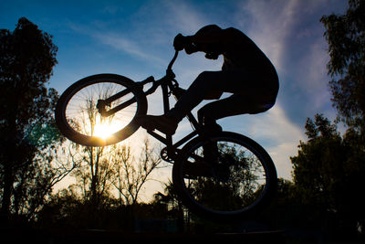 Silhouette man riding bicycle against sky during sunset