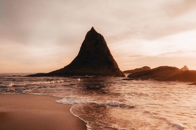 Rock formation on beach against sky during sunset