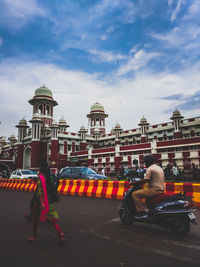 People in front of building against cloudy sky