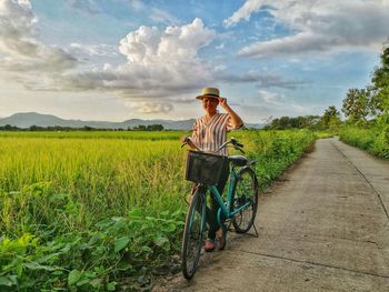 Woman standing by bicycle against agricultural field