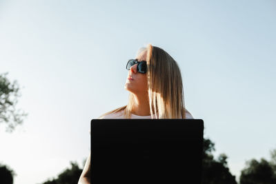 Woman using laptop while sitting against sky
