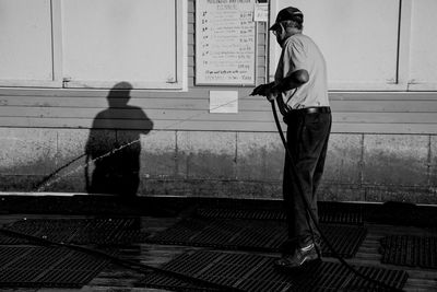 Side view of senior man watering on street against wall