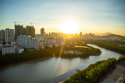 River amidst buildings in city against sky during sunset