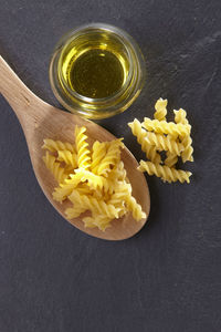 Close-up of fusilli in wooden spoon with oil on slate