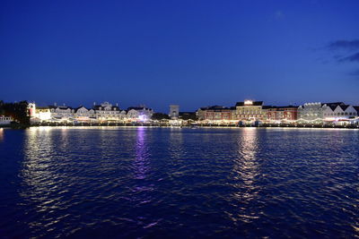 Illuminated buildings by sea against clear sky at night