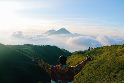 Rear view of man with arms outstretched standing on mountain against sky