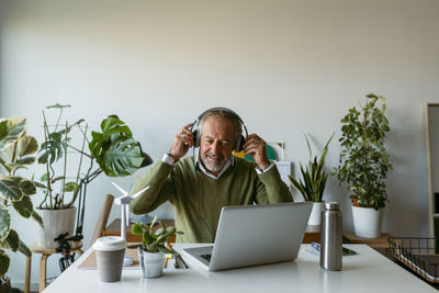 Smiling man wearing headphones while working on laptop at home