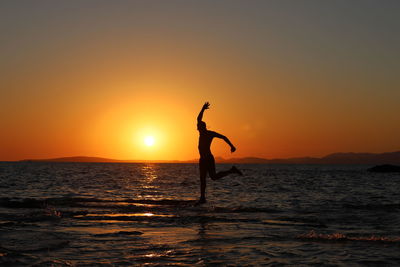 Silhouette woman standing at beach against sky during sunset