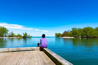 Rear view of woman sitting on lake against blue sky