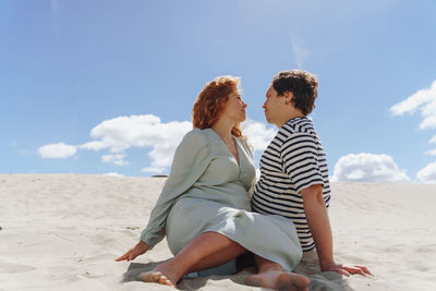 Rear view of couple sitting on beach against sky