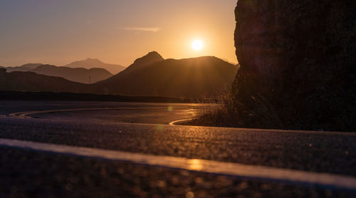 Road by mountains against sky during sunset