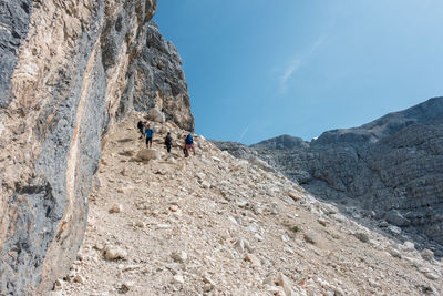 People on cliff by mountains against sky