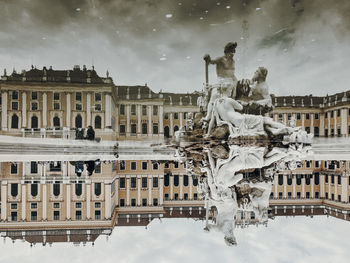 Reflection of buildings and statue in lake against sky in city