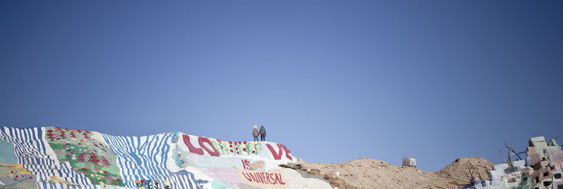 Man and woman standing on cliff with graffiti against clear blue sky