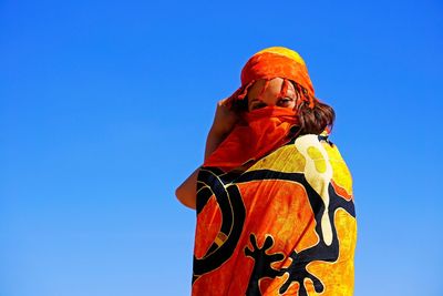 Low angle portrait of woman wrapped in sarong against blue sky