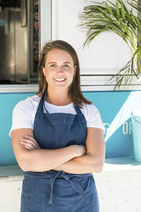 Portrait of smiling young female owner standing with arms crossed against food truck