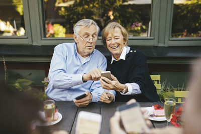 Happy senior couple using mobile phone at outdoor restaurant