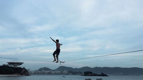 Man walking on rope at beach against sky