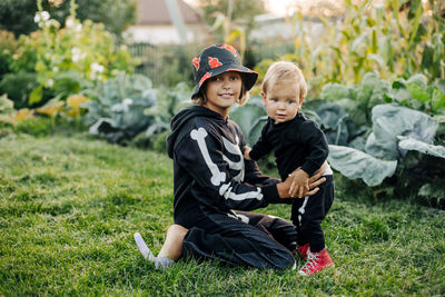 A happy blond boy and his sister in carnival skeleton costumes are playing in the garden 