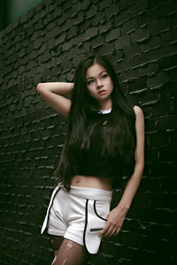 Young woman looking away while standing against wall