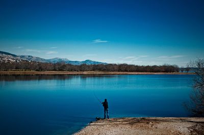 Man fishing on lake against blue sky