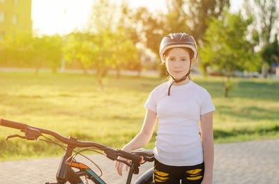 Girl with a bike in the park. an 11-year-old girl in a protective sports helmet next to a bicycle.