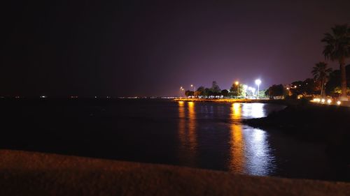 Illuminated buildings by sea against sky at night