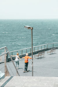 People standing on railing by sea against sky