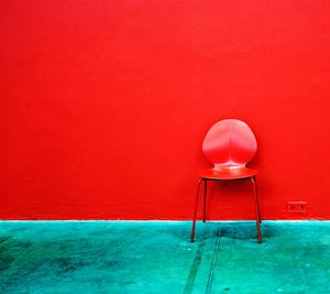 Empty red chair on footpath against wall