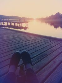 Low section of woman on pier at sunset