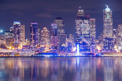 Illuminated modern buildings in city against sky at night