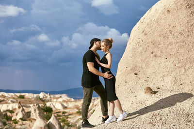 Side view of man standing on rock against sky