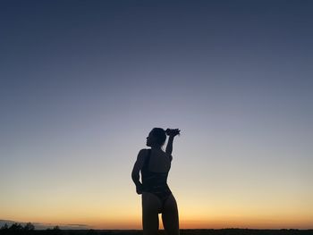 Rear view of silhouette woman standing against clear sky during sunset