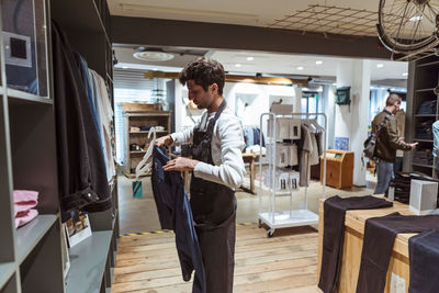 Side view of male owner arranging clothes on shelf at boutique